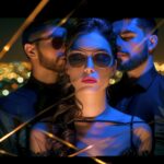 Mujer con gafas de sol rodeada por dos hombres en un ambiente nocturno y sensua