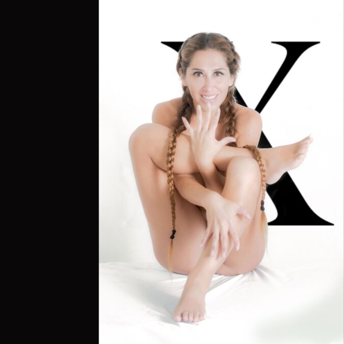 Mujer sentada en pose artística con una gran ‘X’ negra en un fondo blanco minimalista.