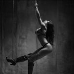 A woman in black lingerie and high boots suspended by chains, exuding power and sensuality.
