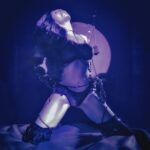Mujer en lencería negra en una postura seductora bajo la luz de la luna, con cadenas y accesorios, durante el evento Jueves Oscuro en OPEN-MINDED