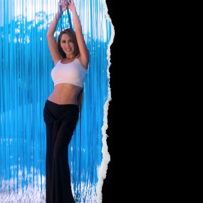 Una mujer sonriente, levantando los brazos en celebración, vestida con un top blanco y pantalones negros, con un fondo de luces de neón y texturas onduladas, promocionando la Fiesta 9 d’Octubre en Open-Minded.