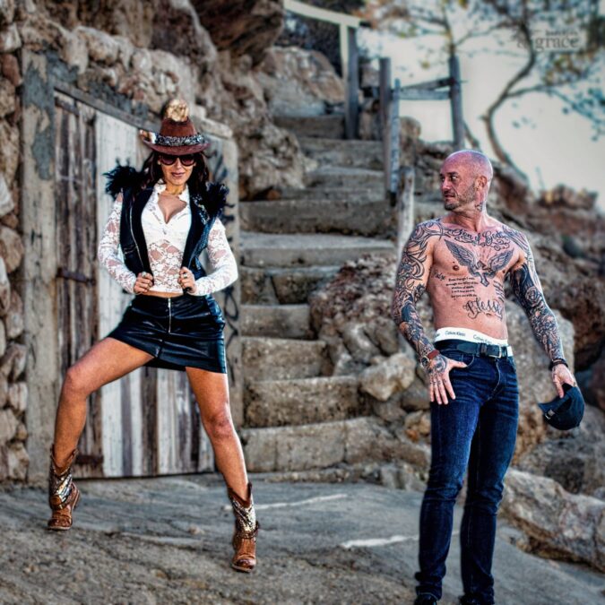 Mujer con estilo audaz y hombre tatuado en un entorno rocoso, rompiendo estereotipos de moda y actitud.